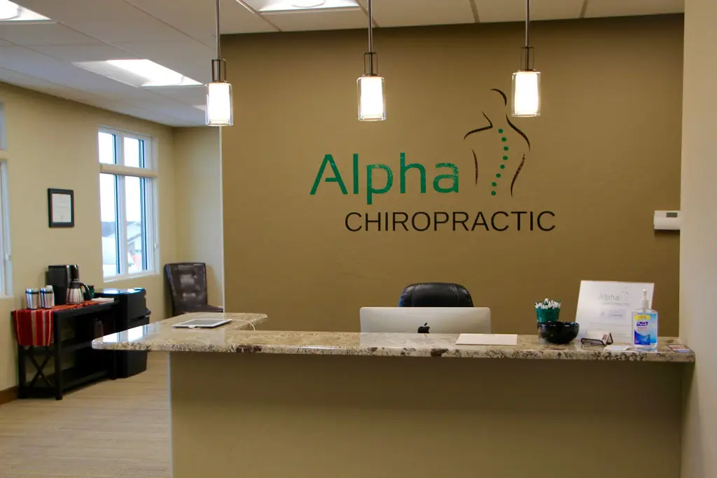 Reception desk at Alpha Chiropractic under the wall-mounted Alpha Chiropractic sign