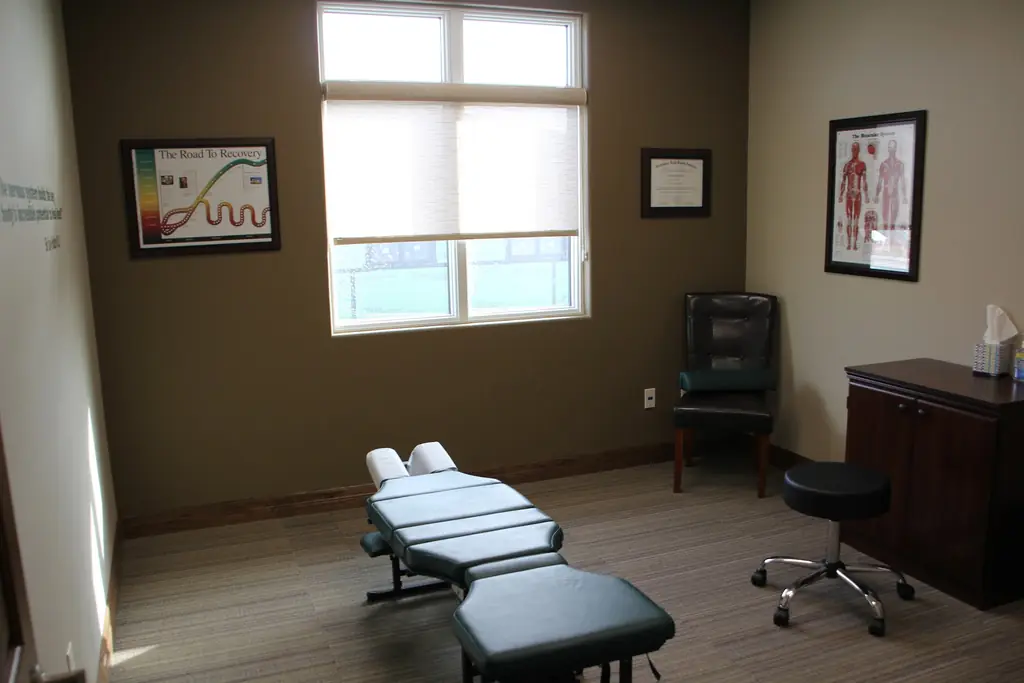 Adjustment table in a treatment room at Alpha Chiropractic, with a framed diploma and anatomical posters on the wall